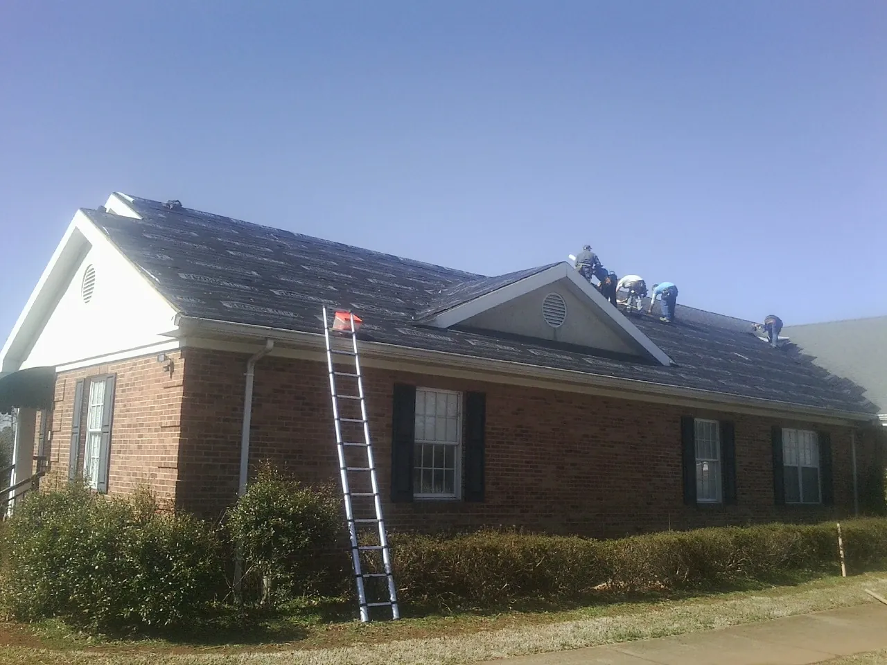 Crew tearing shingles off a brick ranch roof with a ladder set — Emergency Roof Repair work by our crew in Dunreith