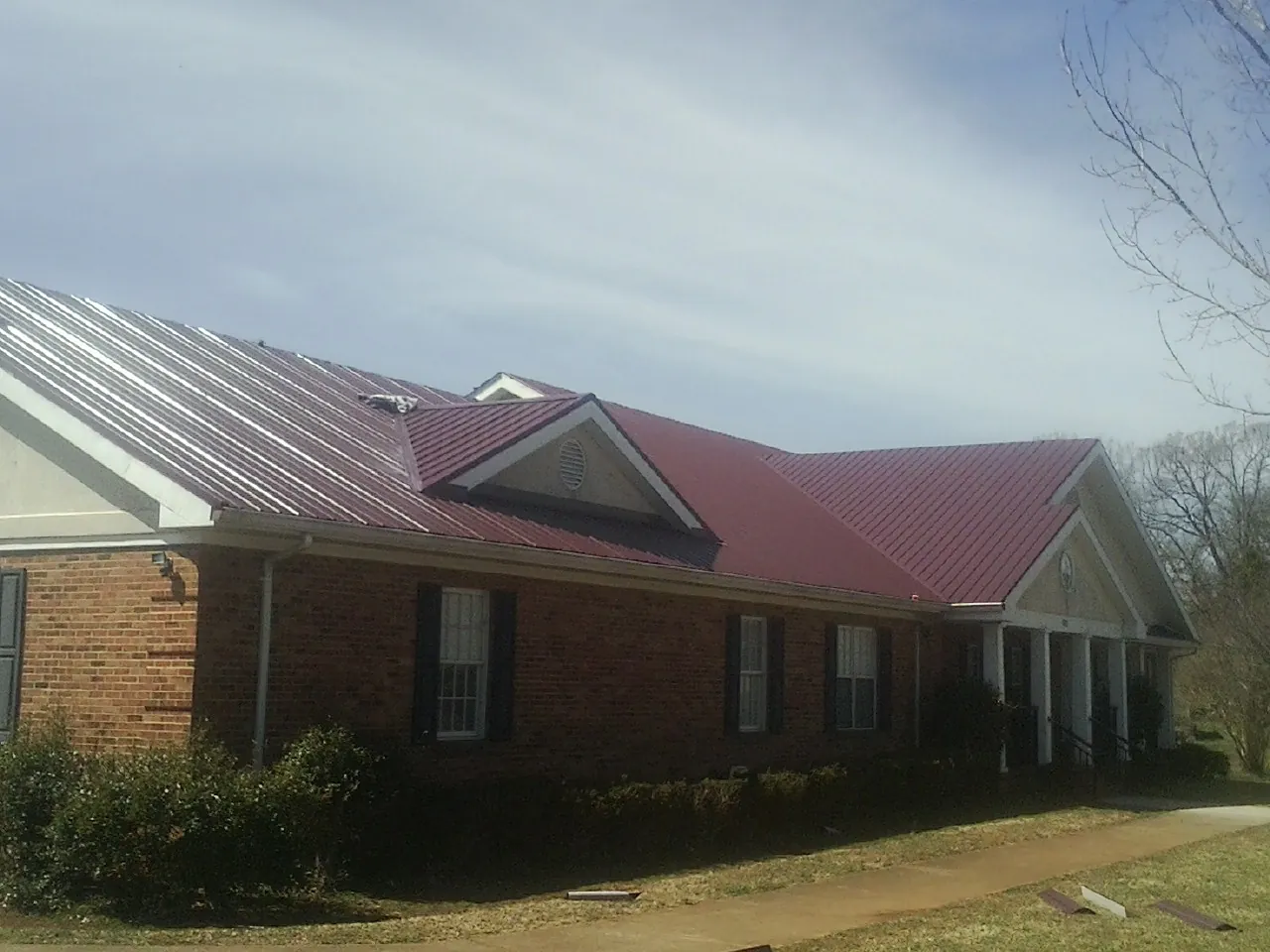 Red metal roof with gabled entries on a long brick building, from a Hail Damage Roof Repair job in Dunreith