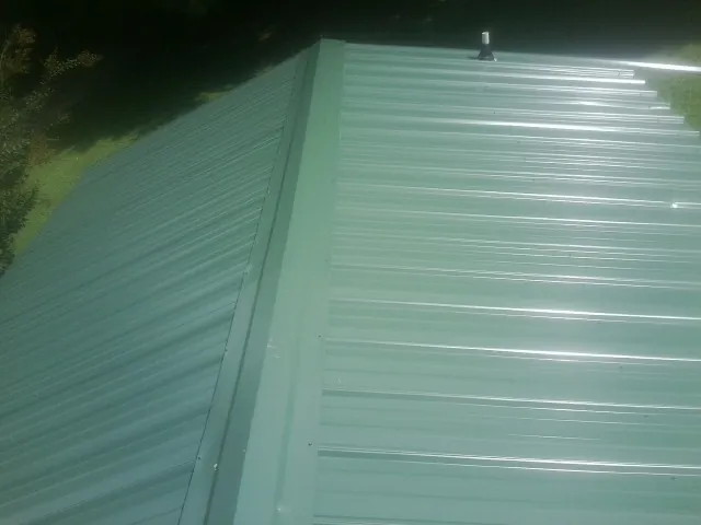New green metal panels meeting at the ridge of a roof — Flat Roof Repair work by our crew in Dunreith