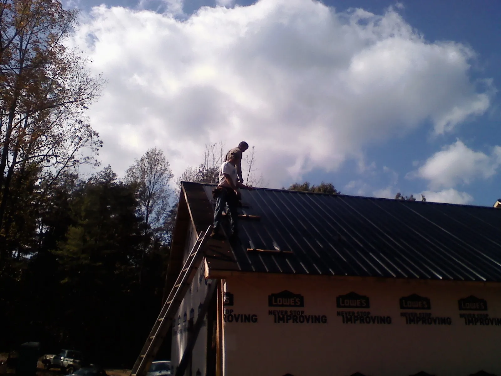 Roofer fastening dark metal panels high against a cloudy sky, from a Roof Inspection job in Dunreith