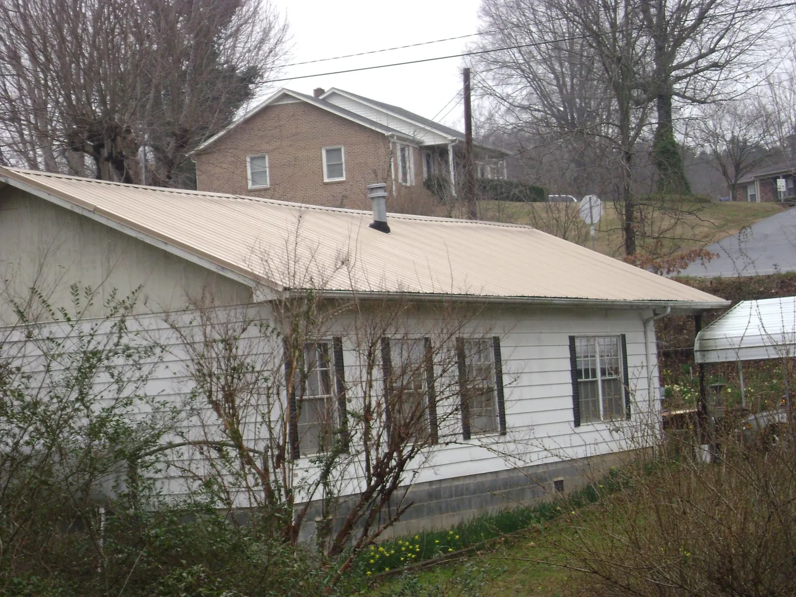 Tan metal roof on a white sided house set into a hillside — Commercial Roofing by Roofing Brothers in Dunreith
